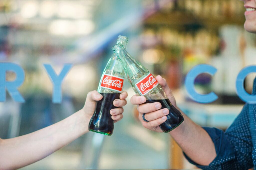 Two people clinking Coca-Cola bottles together, celebrating the 'Share a Coke' campaign.