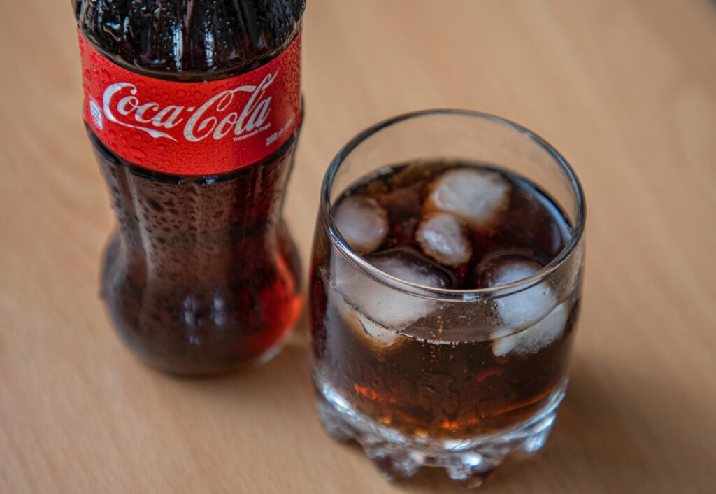 A Coca-Cola bottle next to a glass of Coke with ice, illustrating the brand's iconic colors and visual appeal in sensory branding.