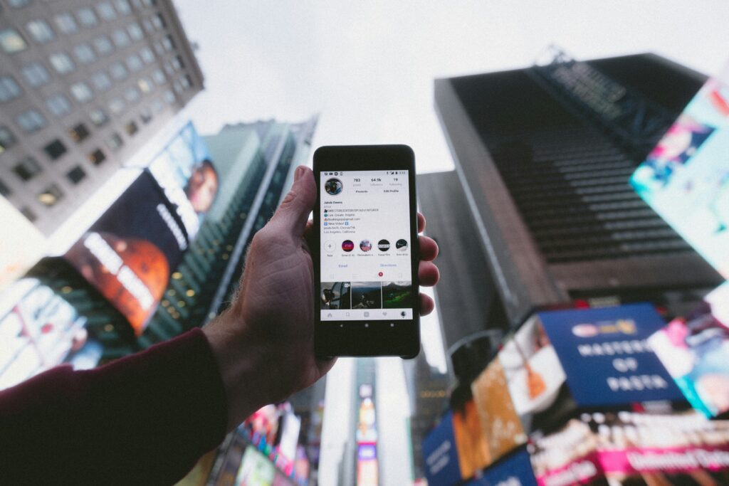 An influencer holding a smartphone and facing upwards against the backdrop of high-rise buildings, representing the digital nature of influencer marketing in urban settings.