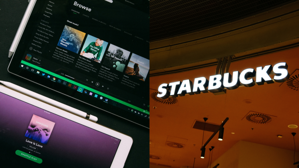 Two Starbucks cups and a smartphone displaying the Spotify app on a wooden table.