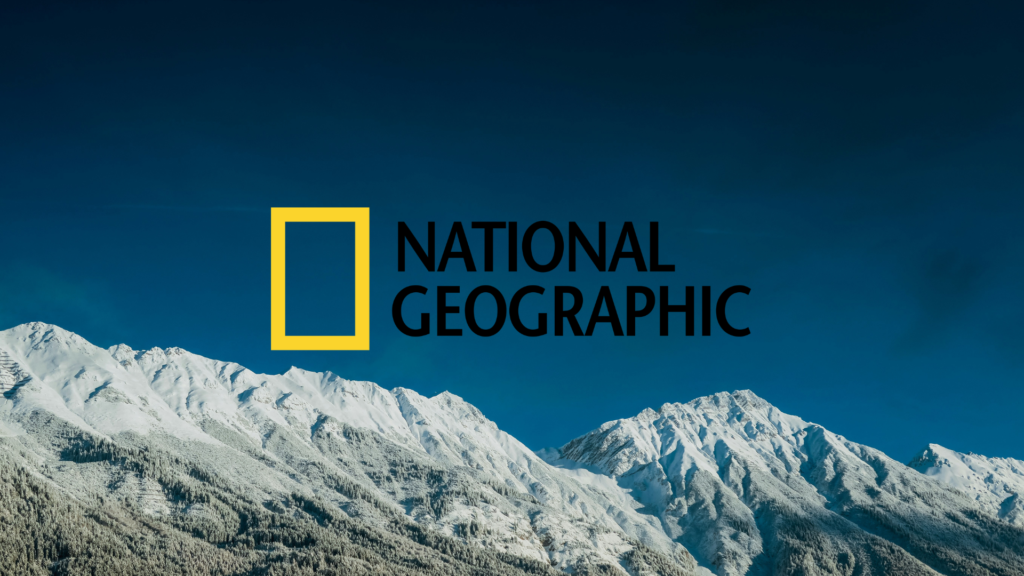 Majestic mountains under a clear blue sky with the National Geographic logo centered at the top, symbolizing exploration and adventure.