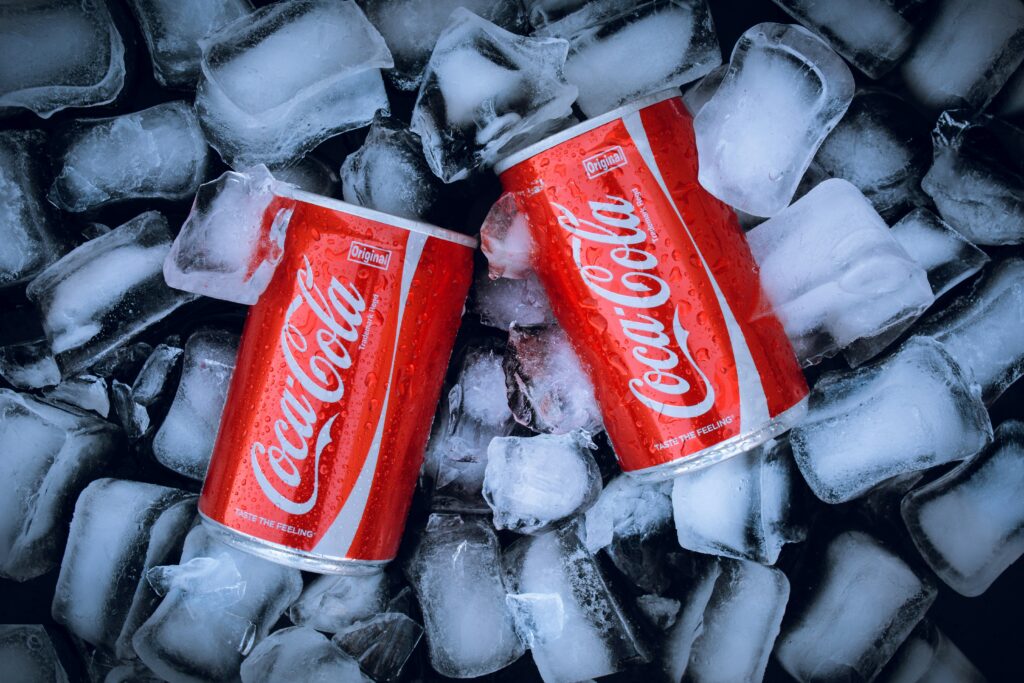 Two Coca-Cola cans resting on ice, showcasing their vibrant and attractive design that highlight the brand's iconic identity.