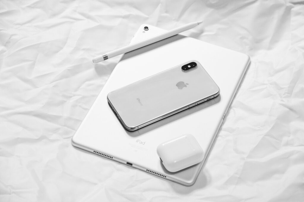 An Apple iPad, iPhone, Apple Pencil, and AirPods displayed together, showcasing Apple's minimalist design aesthetic and product lineup.