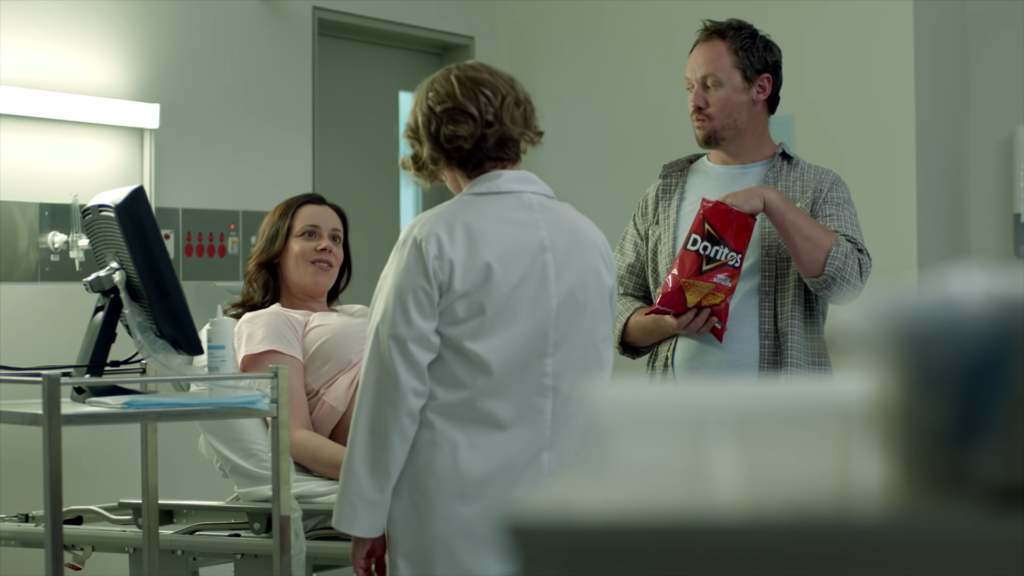 A scene from Doritos' "Ultrasound" ad featuring a pregnant woman during an ultrasound, her husband eating Doritos, and the doctor.