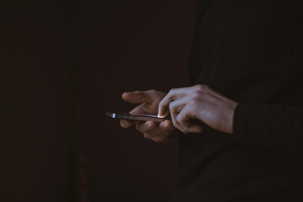 Close-up of a man's hands holding a mobile phone against a black background.