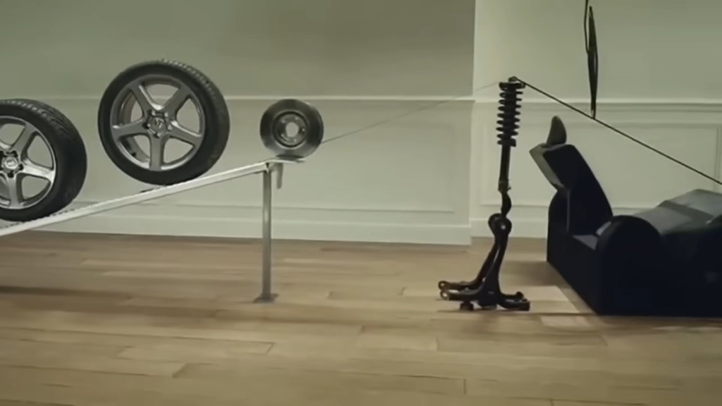 A close-up image from Honda's "Cog" commercial showing a transmission bearing rolling down a board, initiating a chain reaction of car parts.