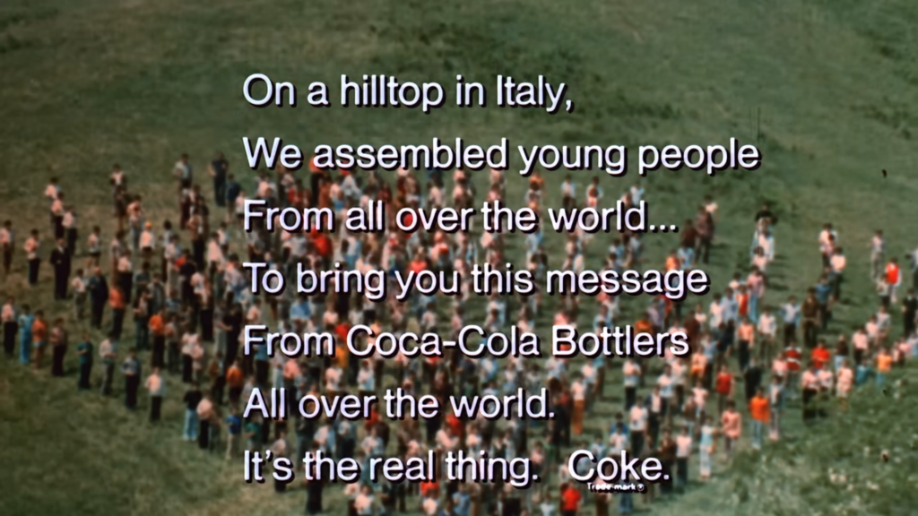 A diverse group of young people standing on a hilltop in Italy from the Coca-Cola Hilltop ad, singing together with bottles of Coca-Cola, representing the message of unity.