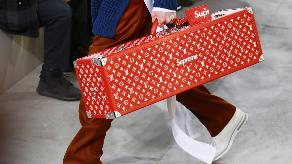 A person carrying a Louis Vuitton x Supreme suitcase, showcasing the unique collaboration between luxury and streetwear.