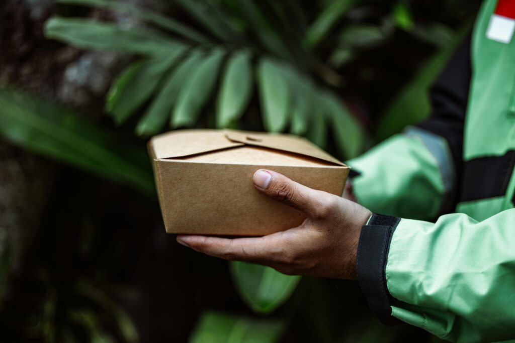 A person holding a sustainably packaged product in one hand, with lush green leaves in the background, symbolizing the importance of eco-friendly practices.