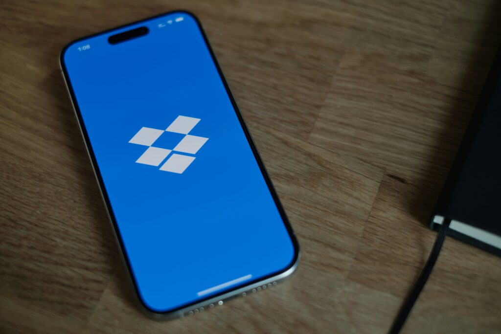 A smartphone placed on a table displaying the Dropbox logo against a clean background, symbolizing cloud storage and file-sharing services.