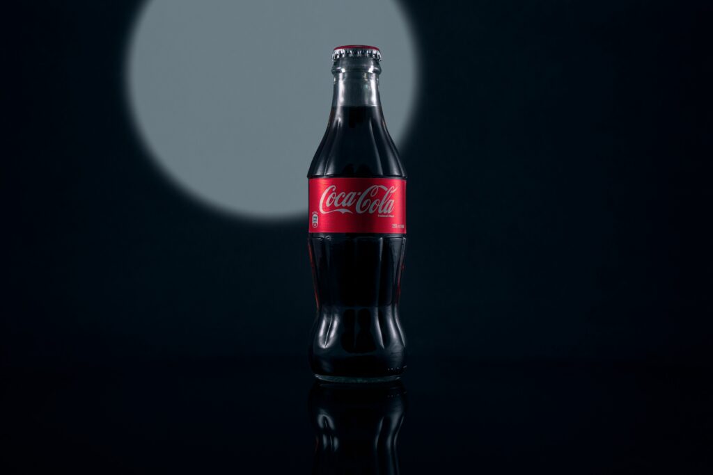 A classic Coca-Cola bottle placed on a table, surrounded by a light background and decorative elements.